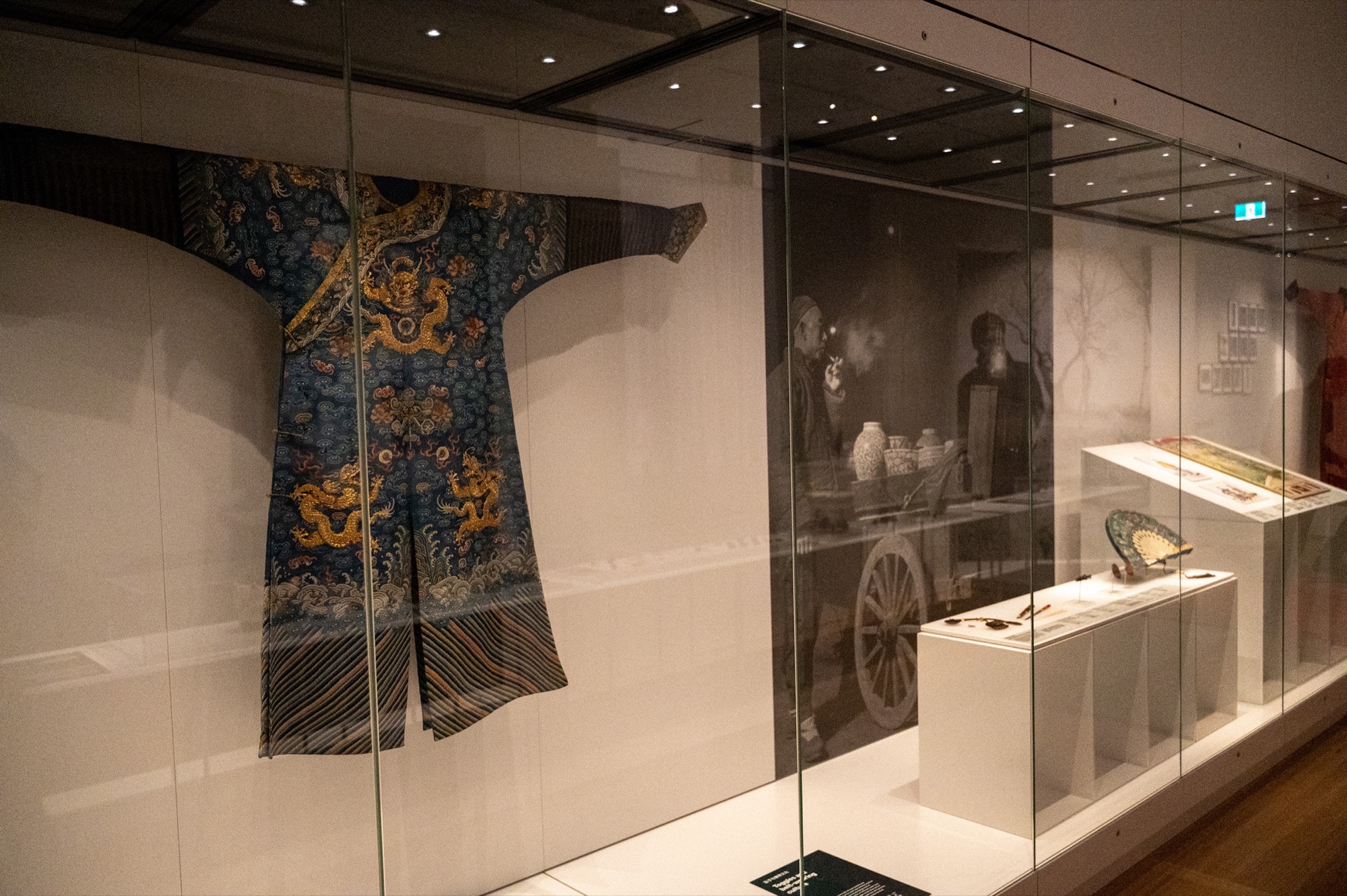 Historic robe displayed beside a full-height exhibition photograph and object labels.