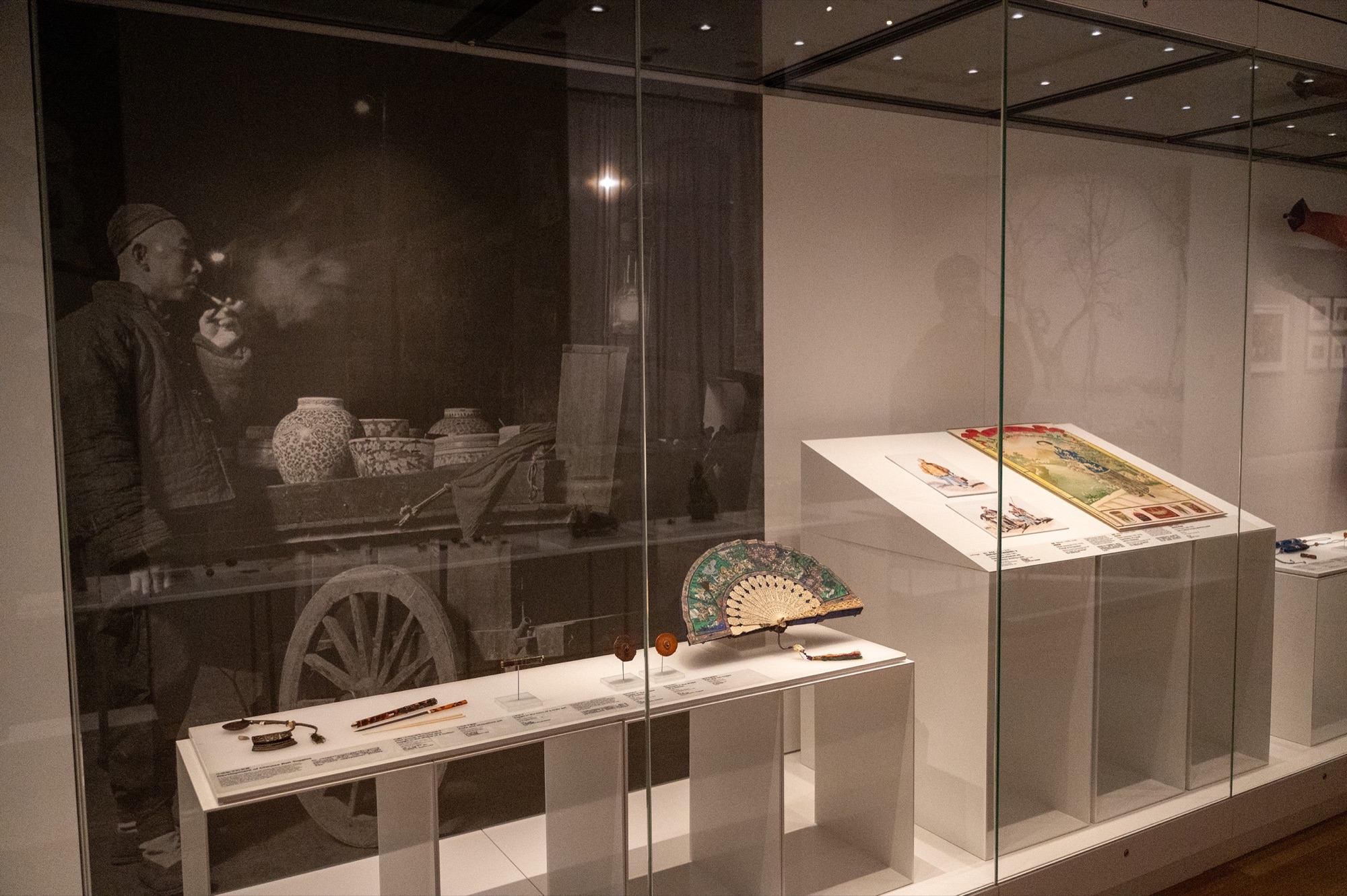Chinese toggles in museum vitrines with a historic cart photograph behind them.