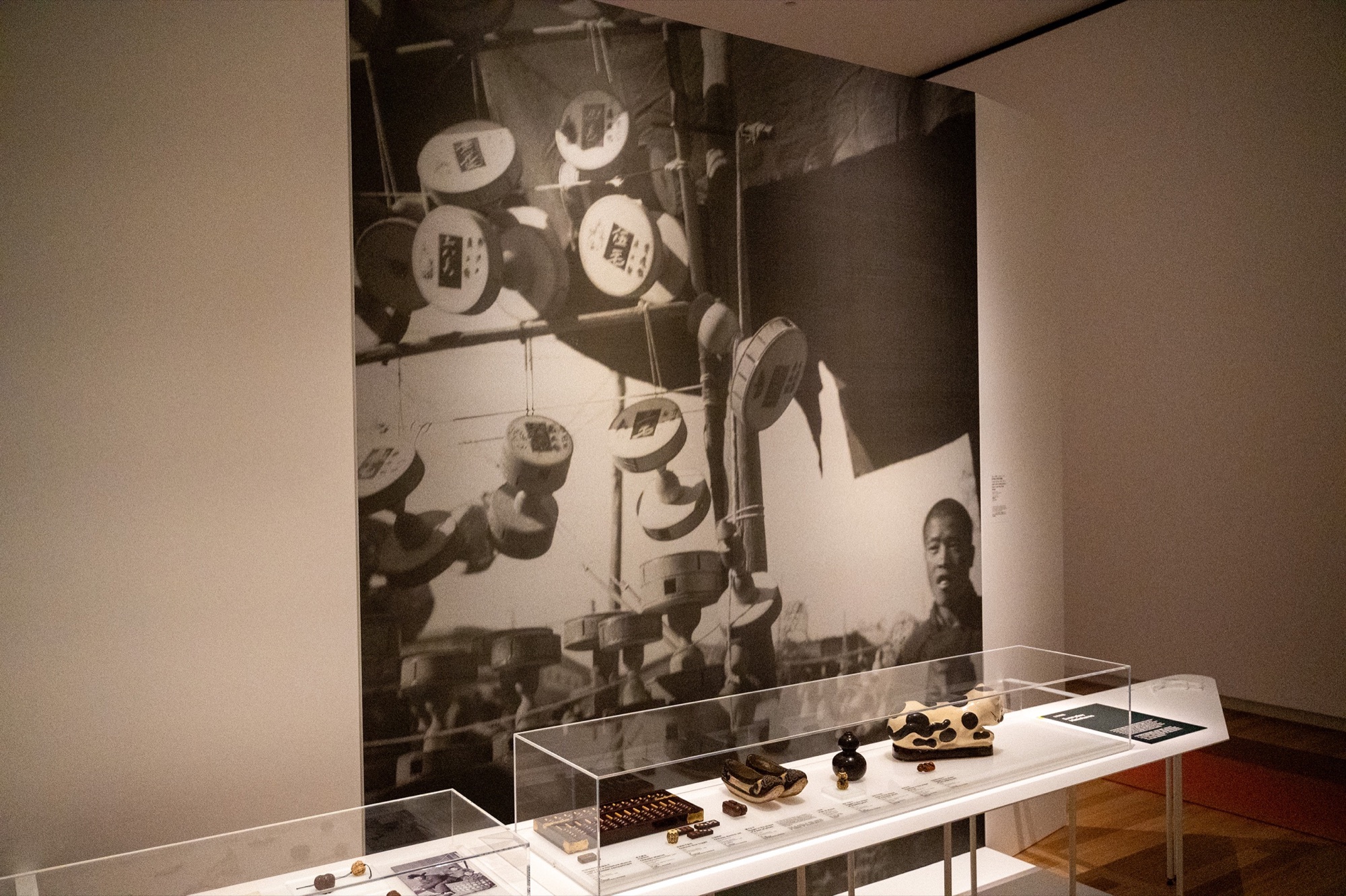 Long object display beneath a full-height monochrome photograph in the Chinese Toggles exhibition.