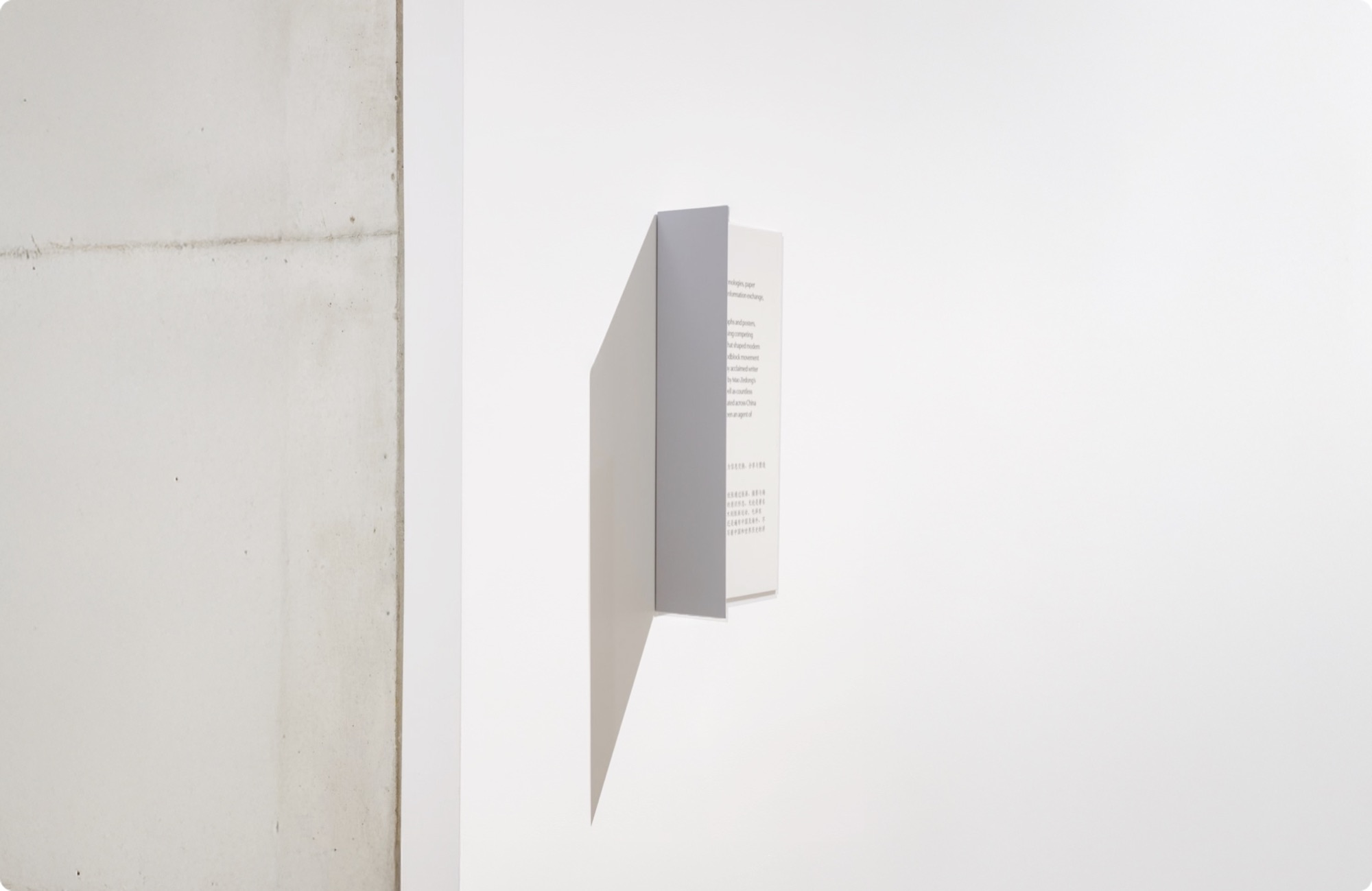 Folded projecting exhibition sign mounted on a concrete gallery wall.